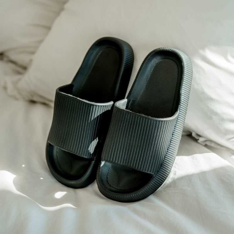 Comfortable black slippers on bed
