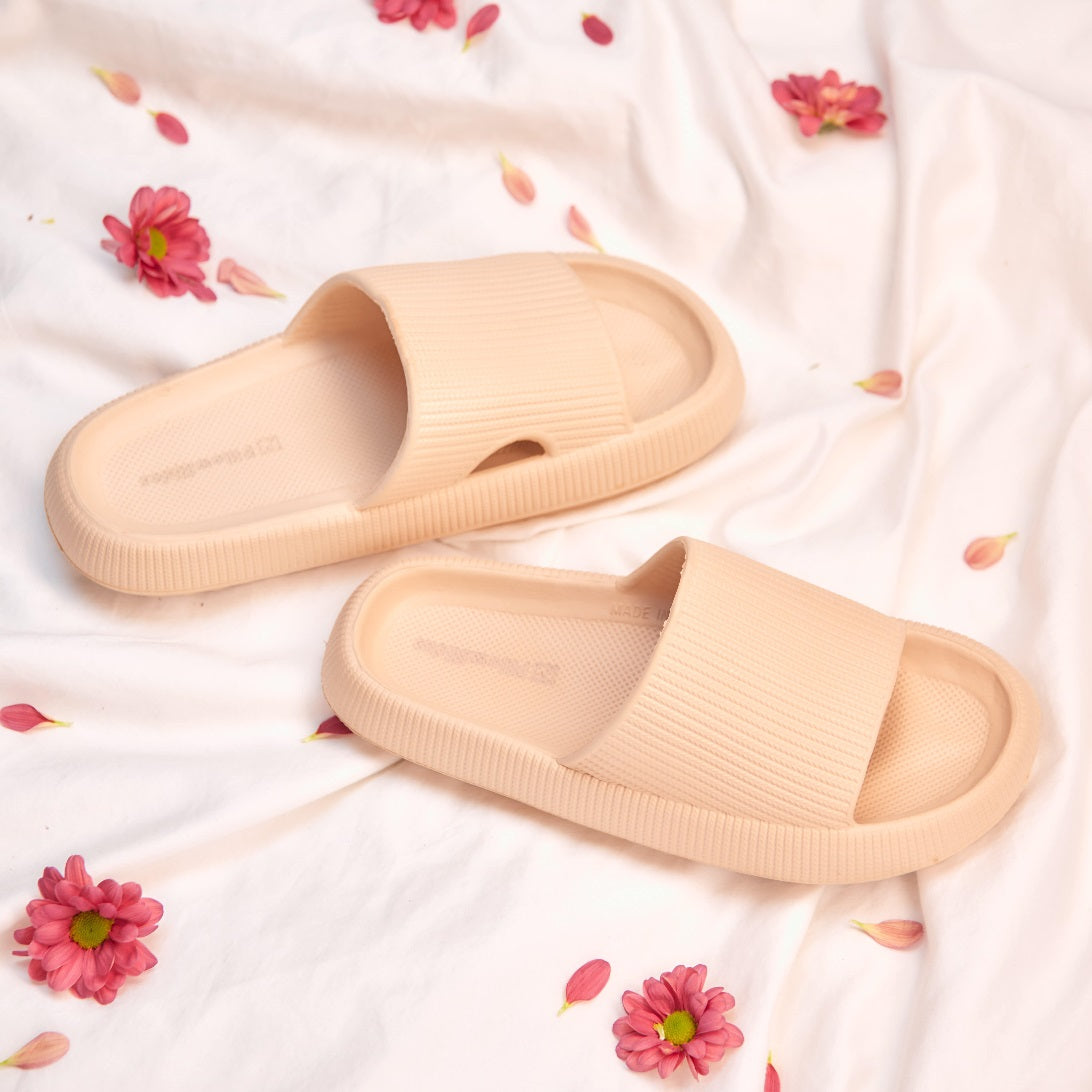 Women's tan slippers on bedding with flowers